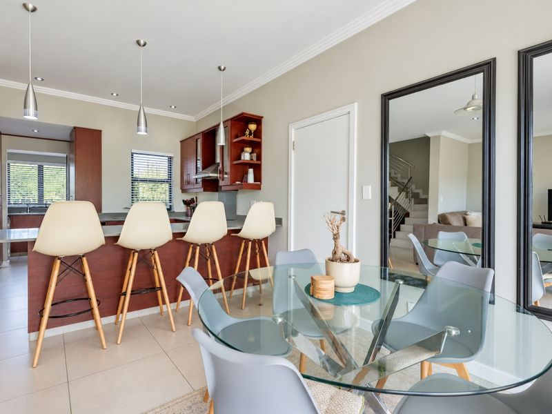 Open-plan kitchen and dining area featuring a breakfast bar, wooden cabinetry, tiled floors, and modern recessed lighting.