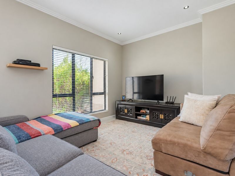 A well-maintained living room featuring neutral wall tones, recessed downlighting, decorative cornice, and a large window with fitted venetian blinds.