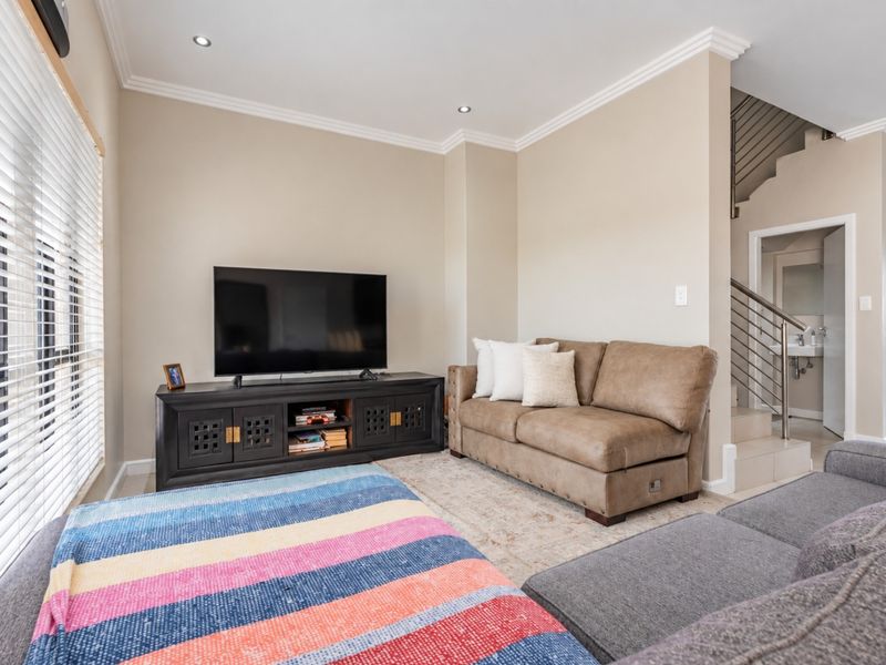 A well-maintained living room featuring recessed downlights, crown molding, and a staircase with a modern metal balustrade, leading to an adjacent bathroom area.