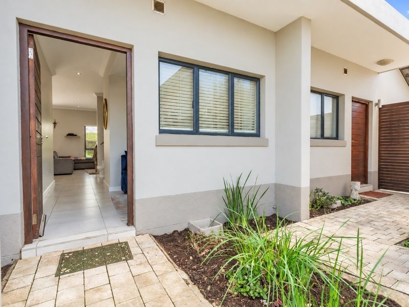 A welcoming townhouse entrance featuring a paved walkway, modern timber door, and clean exterior finishes with tiled flooring visible through the open doorway.