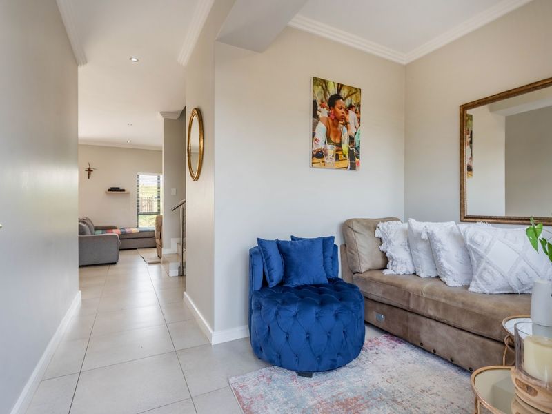 A bright living area featuring neutral walls, tiled flooring, and recessed downlighting, with an open transition to an adjacent living space.