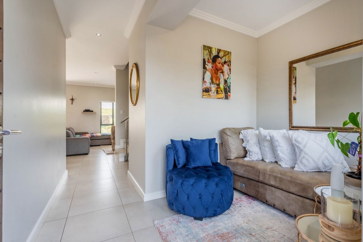 A bright living area featuring neutral walls, tiled flooring, and recessed downlighting, with an open transition to an adjacent living space.