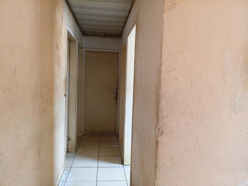 A narrow interior hallway featuring tiled flooring and multiple doorways, showing significant signs of wear and surface staining on the walls.