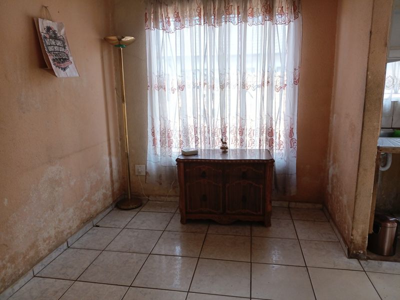 A living area featuring tiled flooring and a window, currently showing significant wall surface deterioration and staining requiring maintenance or renovation.