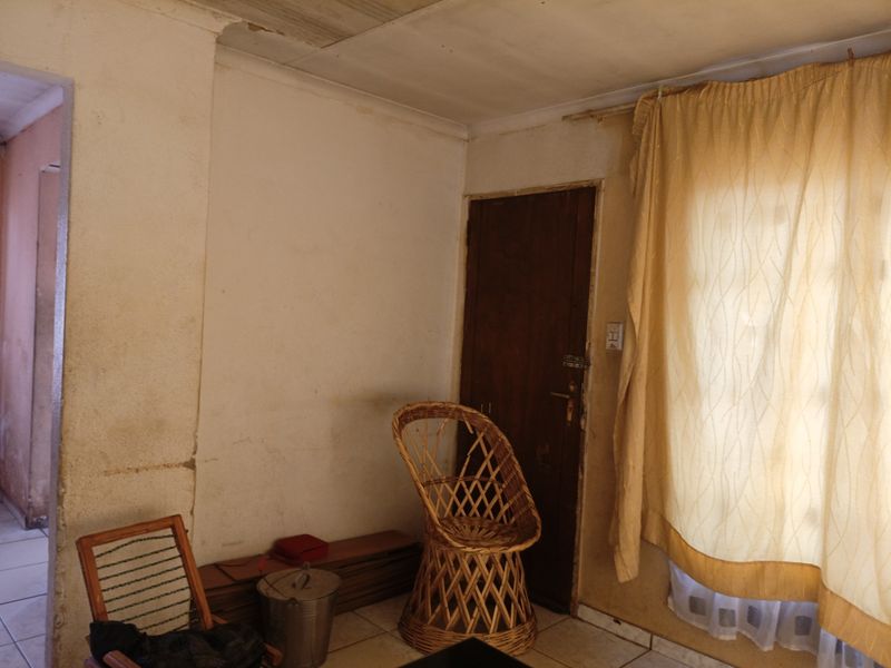 A living area featuring tiled flooring and a timber door, currently showing significant wear to the wall finishes and ceiling.