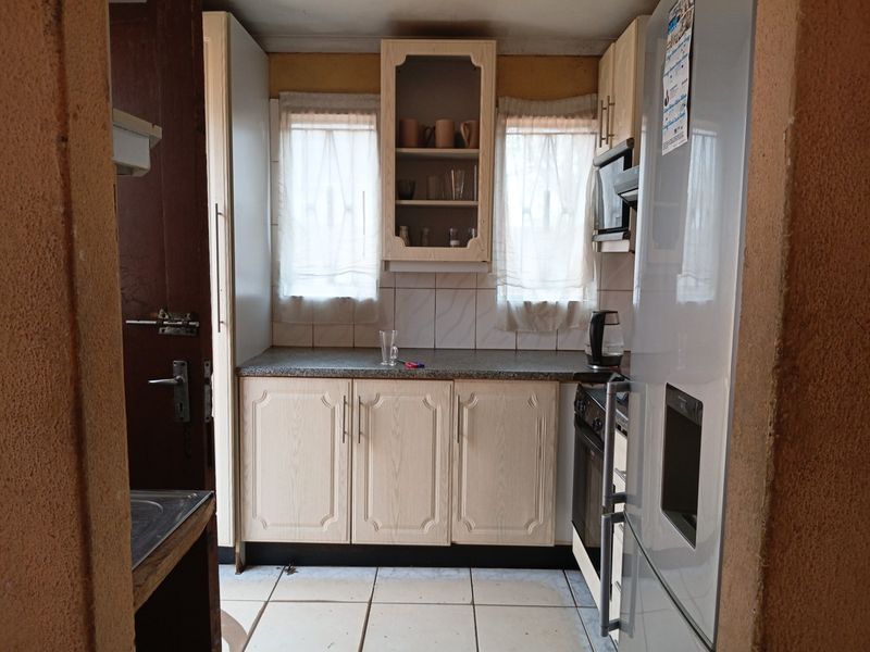 A compact kitchen featuring laminate cabinetry, tiled backsplash, and built-in oven, offering a functional layout in need of cosmetic updates.