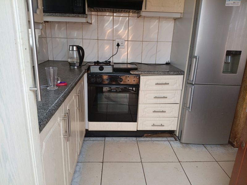 Compact kitchen featuring built-in oven, hob, extractor fan, granite countertops, and tiled finishes, showing signs of wear on the cabinetry.