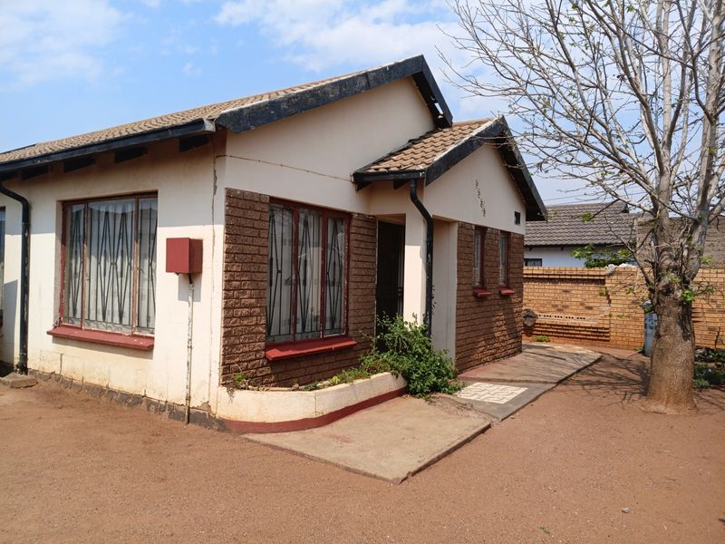 Front view of a single-story house featuring a tiled roof, brick facade, and security bars on windows, set on a compact plot.