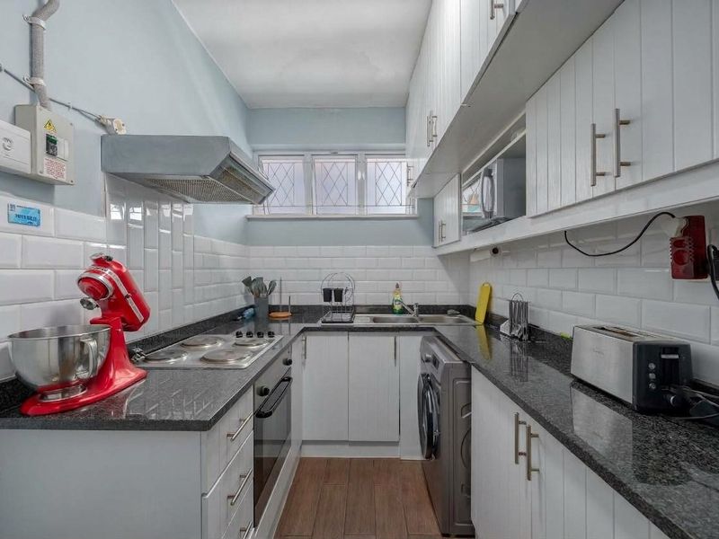 Compact galley kitchen featuring white cabinetry, granite countertops, subway tile backsplash, and integrated appliances, with functional layout and modern finishes.