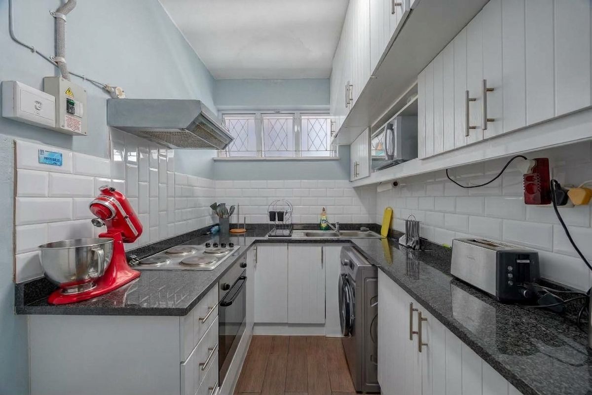 Compact galley kitchen featuring white cabinetry, granite countertops, subway tile backsplash, and integrated appliances, with functional layout and modern finishes.