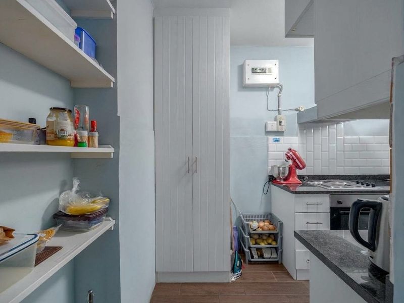 A functional scullery area featuring built-in cabinetry, open shelving, stone countertops, and integrated cooking appliances with a subway tile backsplash.