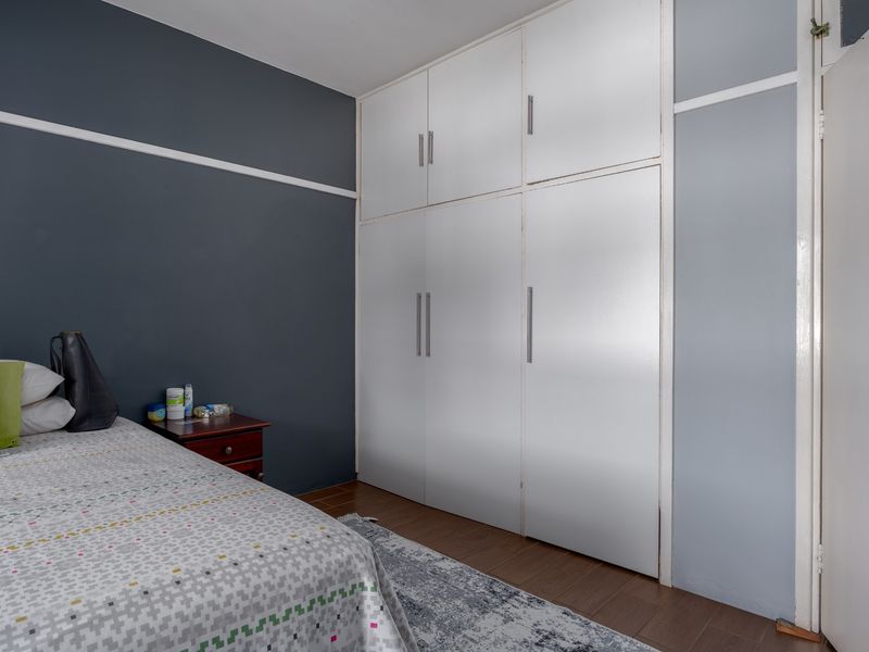 A bedroom featuring dark grey walls, white built-in cupboards with modern handles, and laminate flooring.