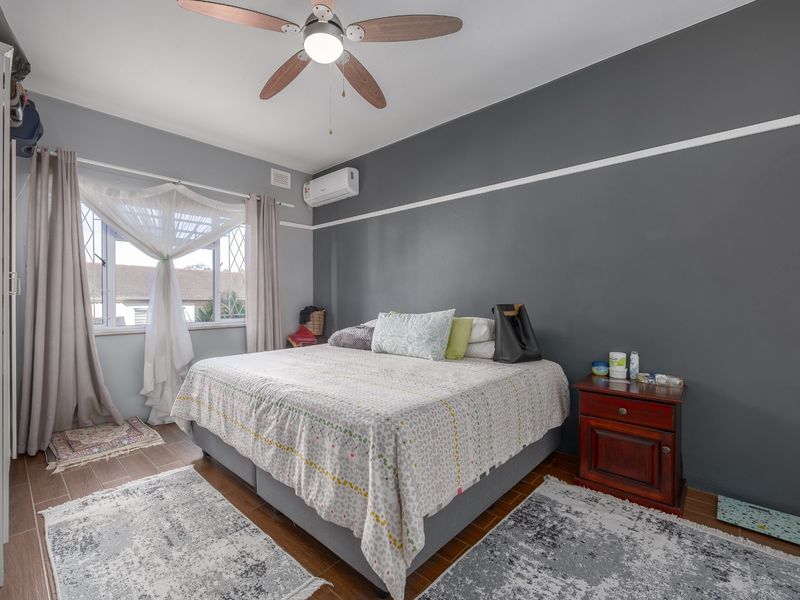 A well-lit bedroom featuring tiled flooring, a ceiling fan, and a wall-mounted air conditioning unit.