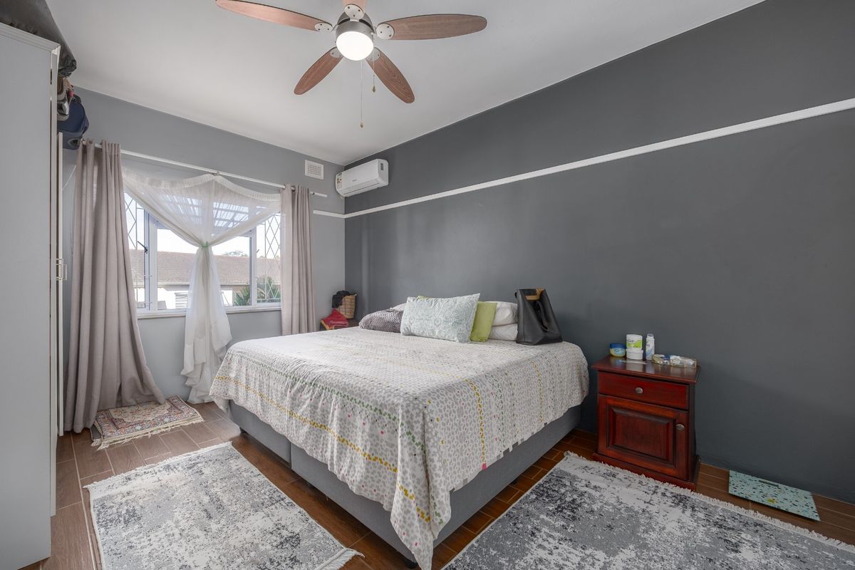 A well-lit bedroom featuring tiled flooring, a ceiling fan, and a wall-mounted air conditioning unit.