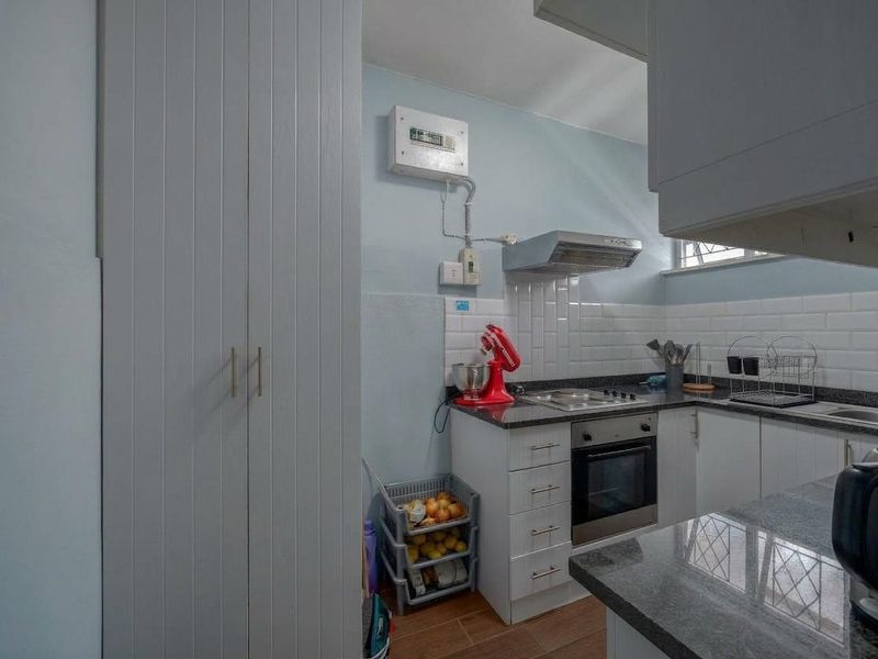 Compact kitchen featuring granite countertops, subway tile backsplash, built-in oven, electric hob, and ample storage cabinetry.