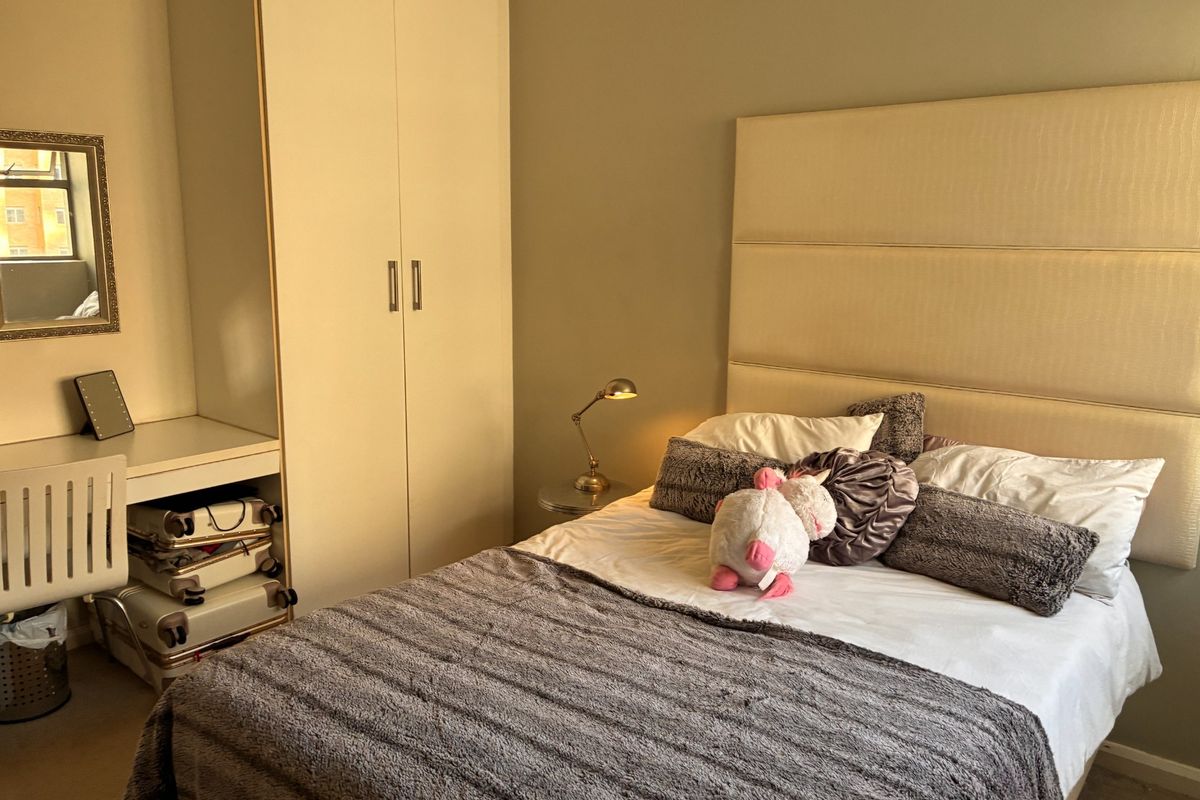 A well-maintained bedroom featuring a built-in wardrobe and integrated desk space with neutral wall finishes and carpeted flooring.