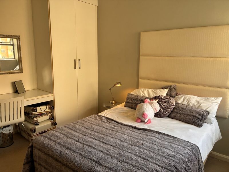 A well-maintained bedroom featuring a built-in wardrobe and integrated desk space with neutral wall finishes and carpeted flooring.