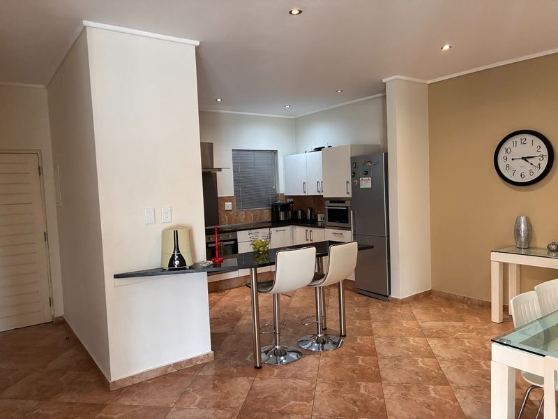 Open-plan kitchen featuring built-in cabinetry, granite countertops, and a breakfast bar, seamlessly flowing into the dining area with tiled flooring throughout.