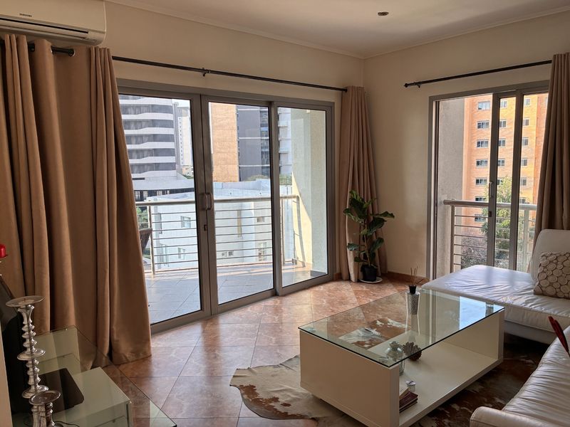 Bright living area featuring large sliding glass doors leading to a balcony, tiled flooring, and a wall-mounted air conditioning unit.