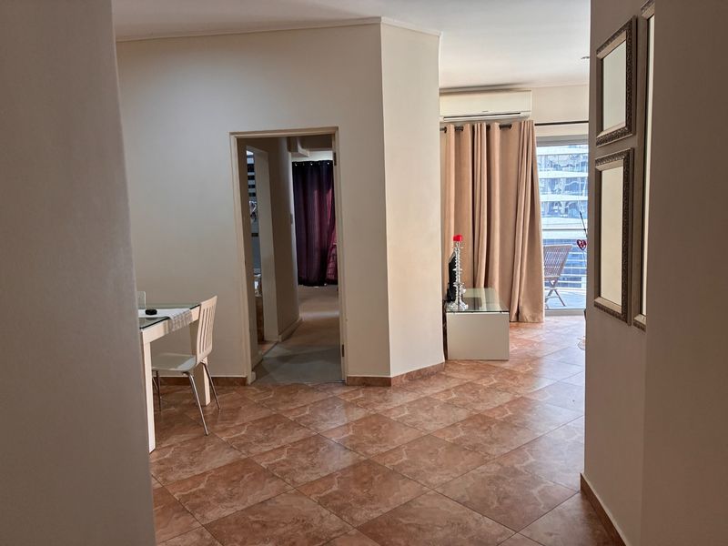 A living area featuring tiled flooring, a wall-mounted air conditioning unit, and direct access to an outdoor balcony through a sliding glass door.