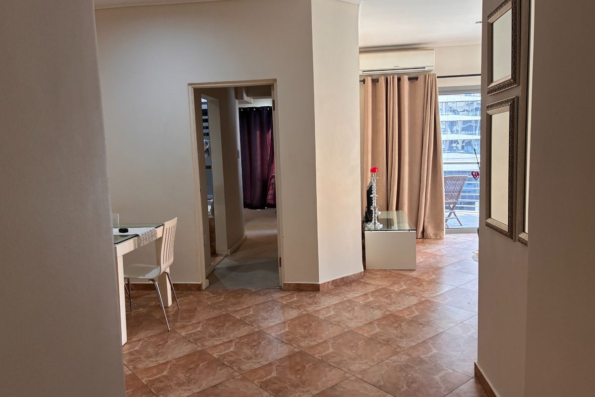 A living area featuring tiled flooring, a wall-mounted air conditioning unit, and direct access to an outdoor balcony through a sliding glass door.