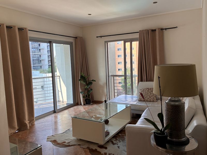 A bright living room featuring tiled flooring and dual sliding glass doors that open onto a balcony with urban views.