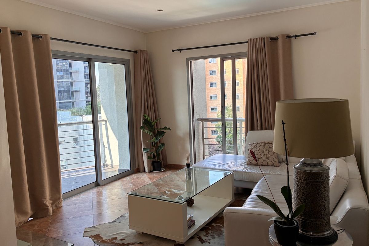 A bright living room featuring tiled flooring and dual sliding glass doors that open onto a balcony with urban views.