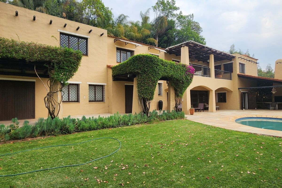 Spacious rear exterior featuring a swimming pool, covered patio area, balcony, and traditional stucco facade with mature landscaping.