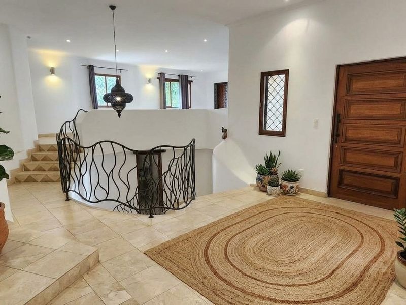 Spacious entrance foyer featuring tiled flooring, a decorative wrought iron balustrade, and a solid timber front door leading to an open-plan living area.