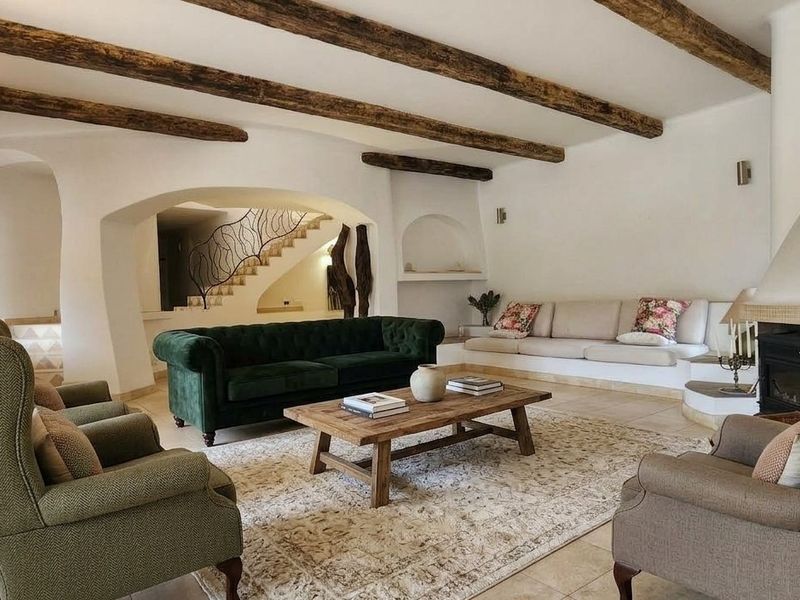 Spacious living room featuring exposed timber ceiling beams, a built-in fireplace, and elegant arched architectural details leading to a staircase.
