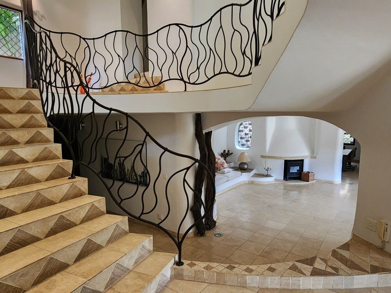 Spacious living area featuring a unique wrought iron staircase, tiled flooring, and a built-in fireplace with distinctive arched architectural design elements.