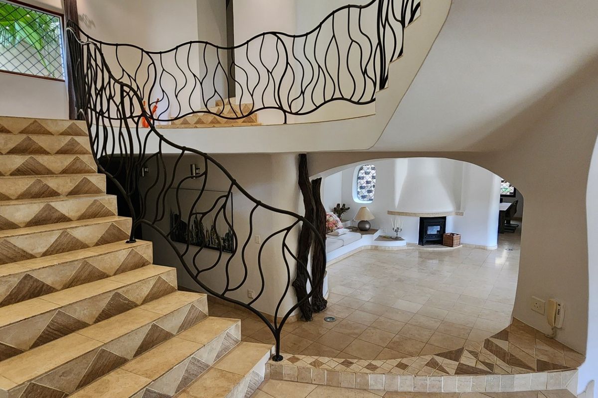 Spacious living area featuring a unique wrought iron staircase, tiled flooring, and a built-in fireplace with distinctive arched architectural design elements.