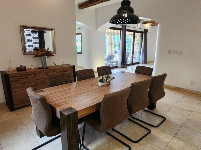 Spacious dining room featuring tiled flooring, exposed ceiling beams, and a cozy wood-burning stove, with arched access to the patio area.