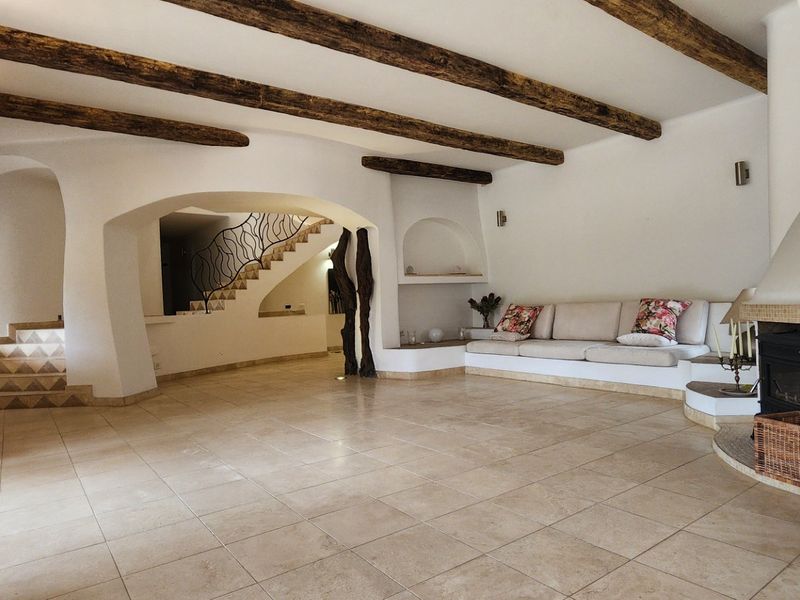 Spacious living room featuring exposed timber ceiling beams, tiled flooring, a built-in fireplace, and unique arched architectural details leading to a staircase.