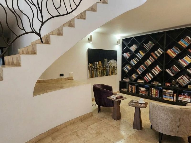 A well-appointed living area featuring a striking wrought iron staircase railing, stone stairs, and a large, custom built-in bookshelf with integrated lighting.