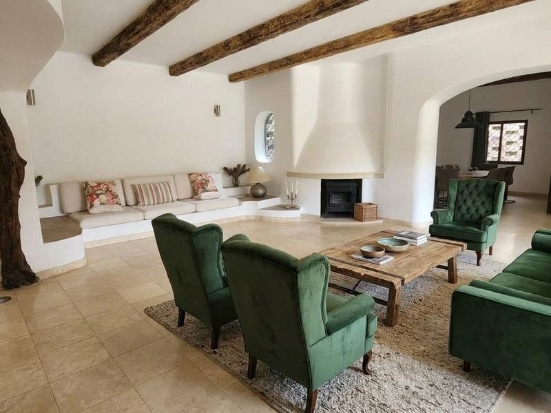 Spacious living room featuring exposed timber ceiling beams, stone tile flooring, and a characterful built-in fireplace with arched architectural details.