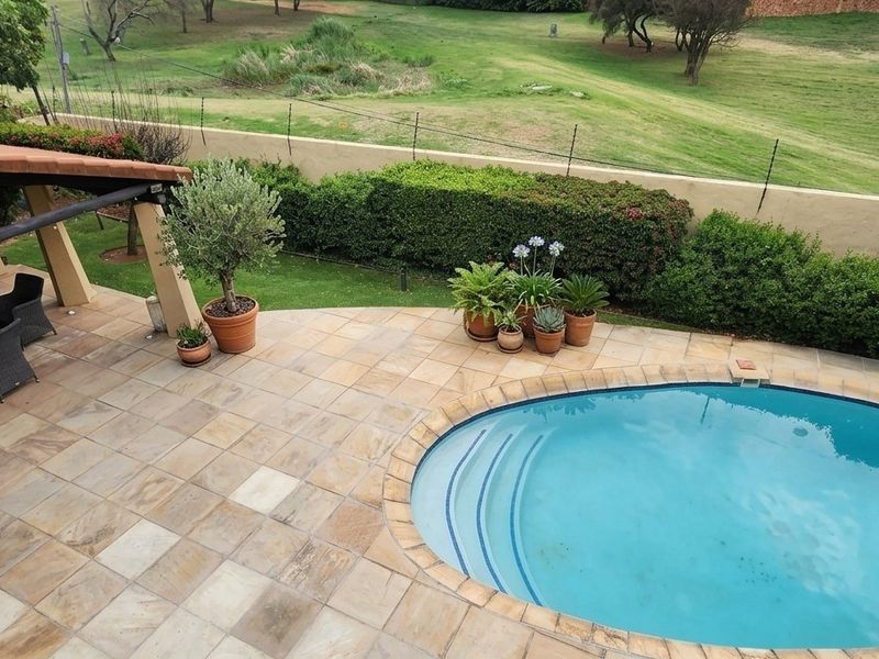 Outdoor entertainment area featuring a paved patio with a covered section and a swimming pool, overlooking a landscaped garden and boundary wall.