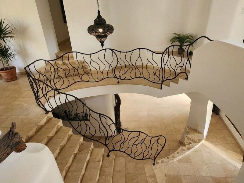 Elegant curved staircase featuring custom wrought iron railings and neutral tiled flooring, creating a sophisticated architectural focal point in the home's entryway.