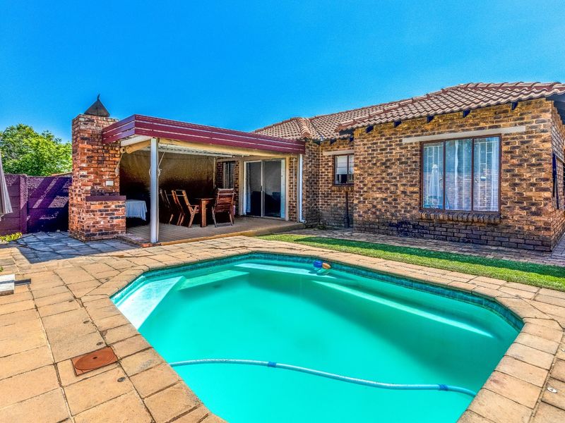 Rear exterior view featuring a swimming pool, paved patio area, and a covered outdoor entertainment space with a built-in brick braai.
