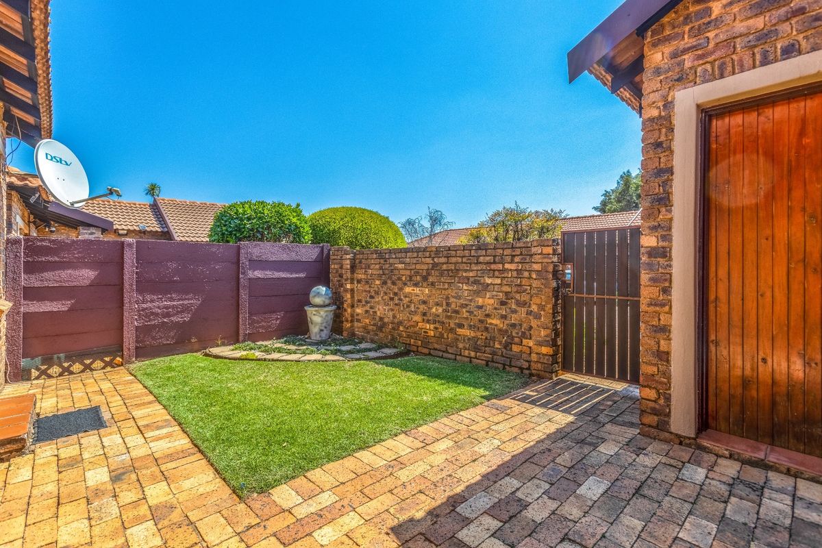 A well-maintained rear courtyard featuring brick paving, a small lawn area, and secure boundary walls with a wooden pedestrian gate.