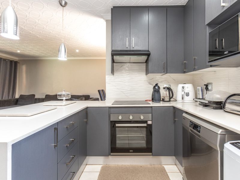 Modern kitchen featuring dark grey cabinetry, stone countertops, built-in oven, hob, extractor fan, and integrated appliances, seamlessly flowing into the adjacent living area.