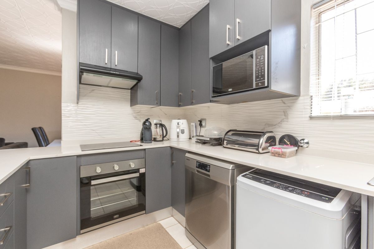 Modern kitchen featuring dark grey cabinetry, stone countertops, built-in oven, hob, extractor fan, and a textured tile backsplash.
