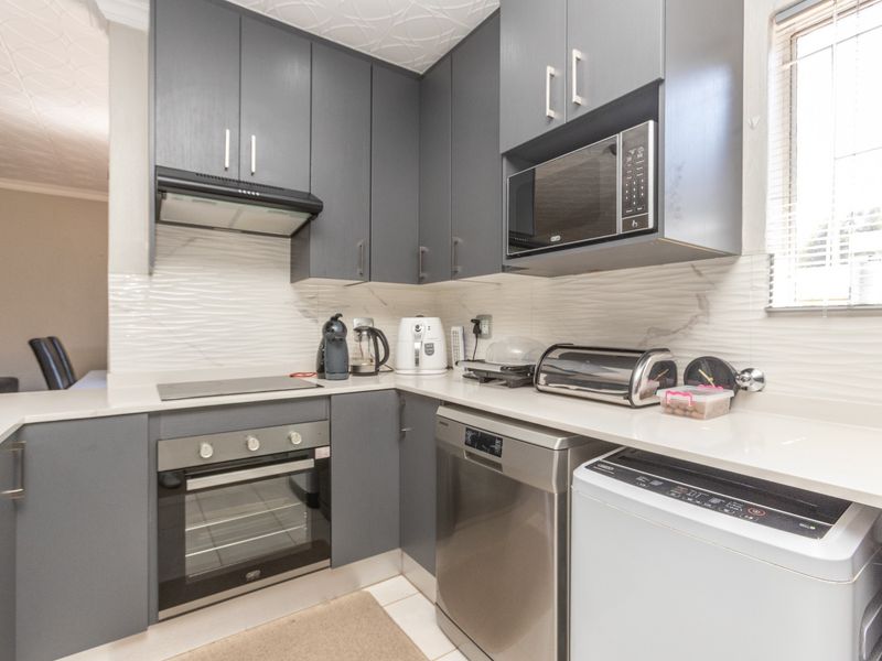 Modern kitchen featuring dark grey cabinetry, stone countertops, built-in oven, hob, extractor fan, and a textured tile backsplash.