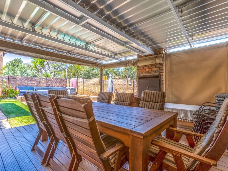 Covered outdoor patio featuring timber decking, a built-in brick fireplace, and retractable canvas blinds, overlooking a private garden area.