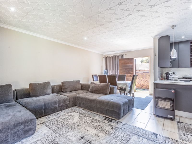 Open-plan living and dining area featuring tiled floors, patterned ceiling tiles, and a modern kitchen with dark cabinetry and integrated lighting.