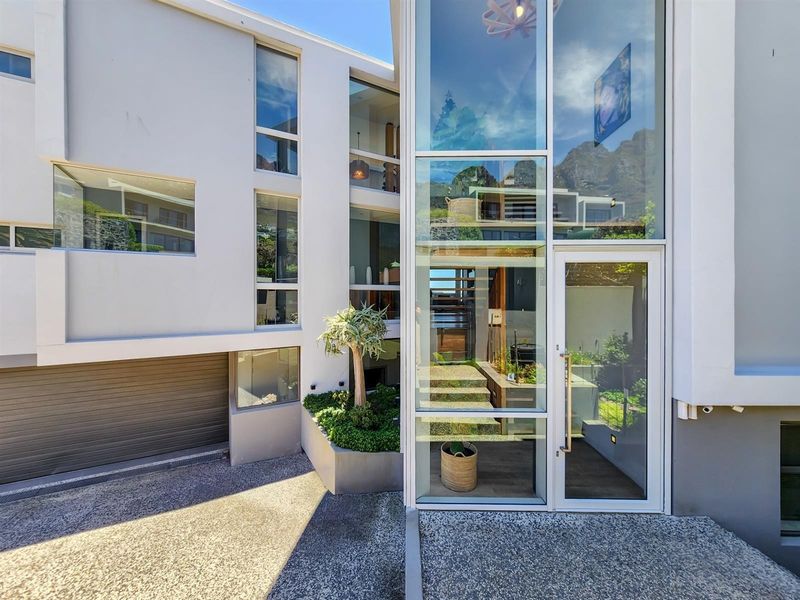 Modern architectural front facade featuring a striking double-height glass entrance, clean lines, and a paved driveway with integrated landscaping.