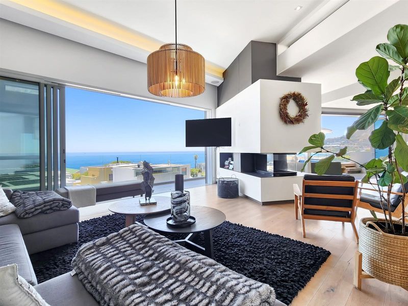 Modern open-plan living area featuring a contemporary built-in fireplace, hardwood flooring, and expansive sliding glass doors offering panoramic ocean views.