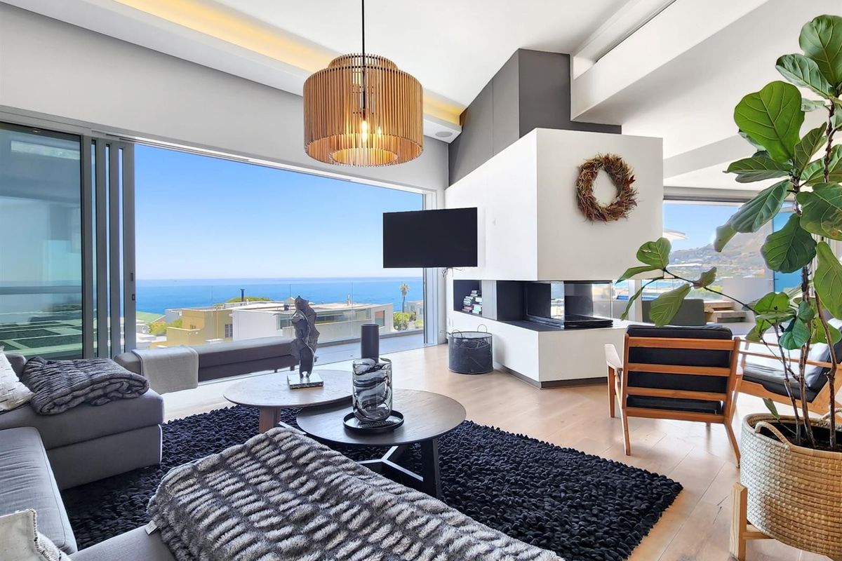 Modern open-plan living area featuring a contemporary built-in fireplace, hardwood flooring, and expansive sliding glass doors offering panoramic ocean views.