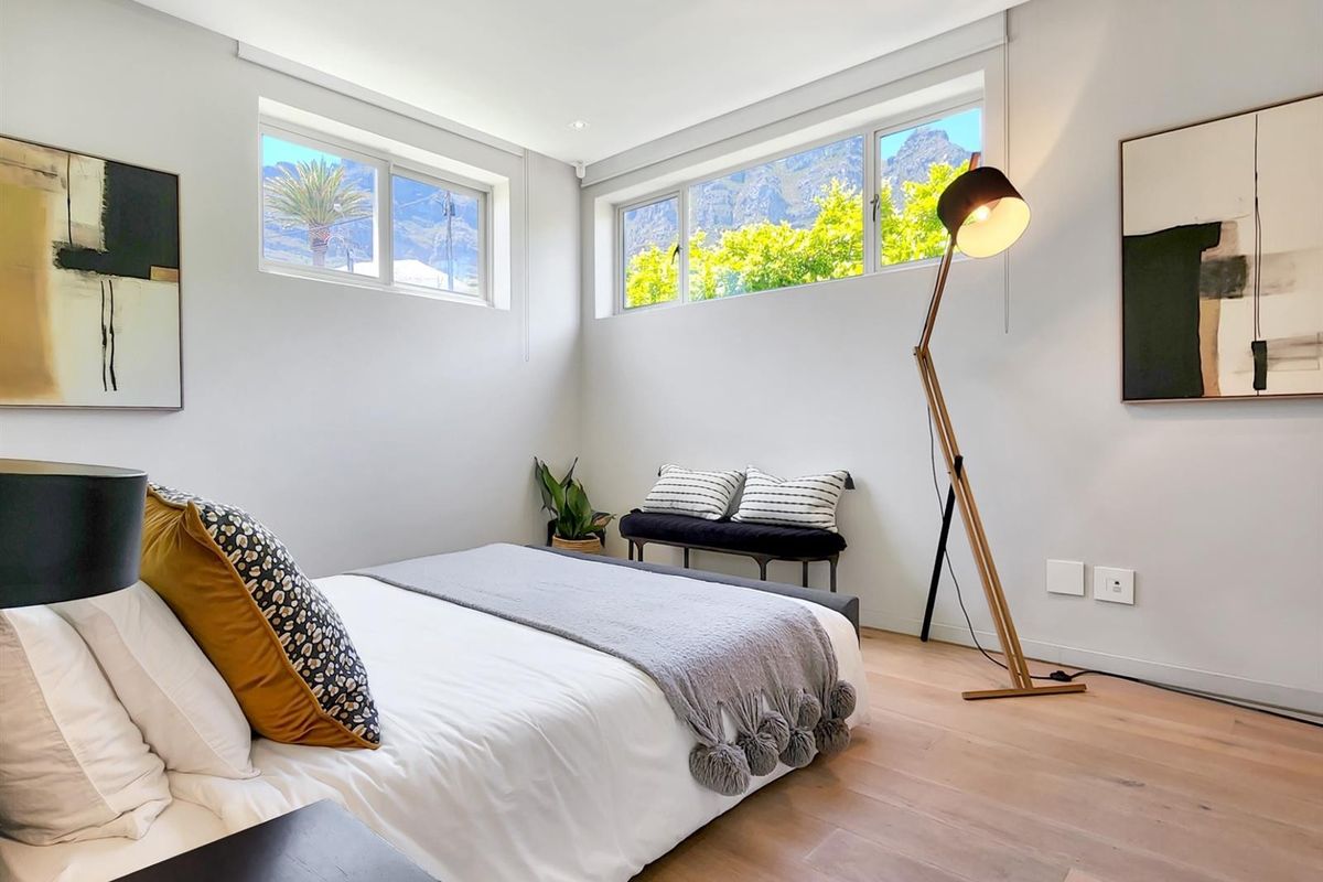 A bright, modern bedroom featuring light timber flooring, neutral walls, and horizontal windows offering scenic mountain views.