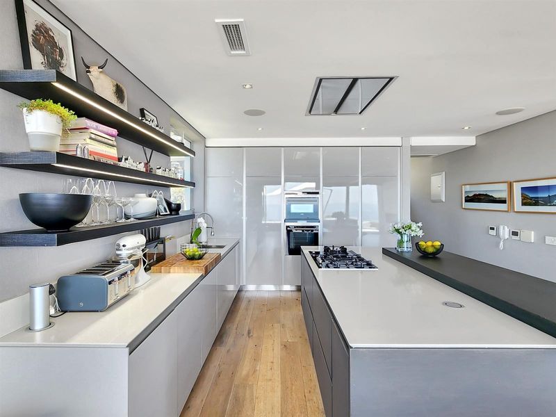 Modern kitchen featuring sleek cabinetry, stone countertops, a central island with gas cooktop, integrated appliances, and stylish floating shelving with under-cabinet lighting.